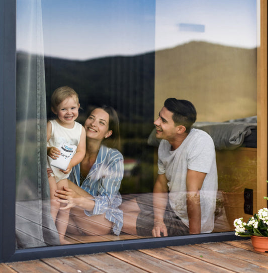 Une famille souriante derrière une vitre propre, reflétant un paysage naturel.